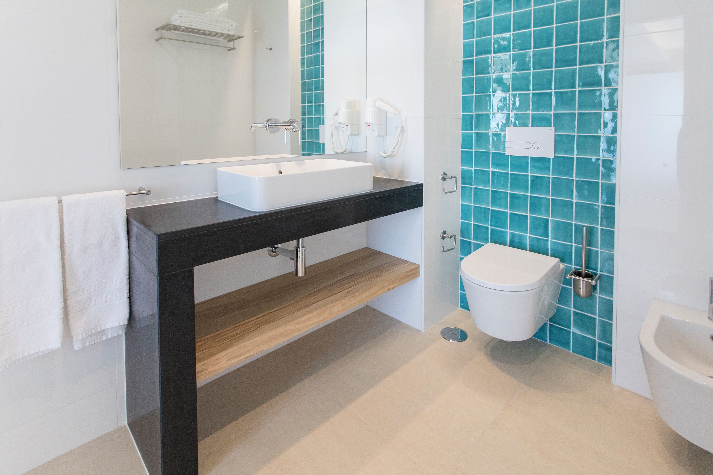A modern bathroom with a black countertop, white sink, and a blue-tiled wall.