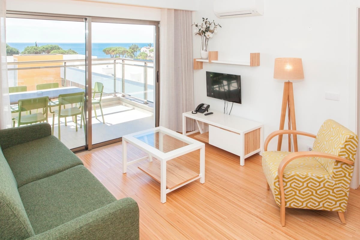 Una sala moderna con sofá, un sillón estampado, una mesa de centro, televisor y lámpara.