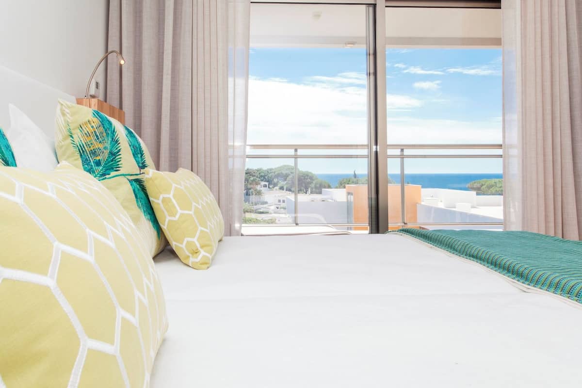 Un dormitorio con cama, cortinas, vista al mar y balcón.