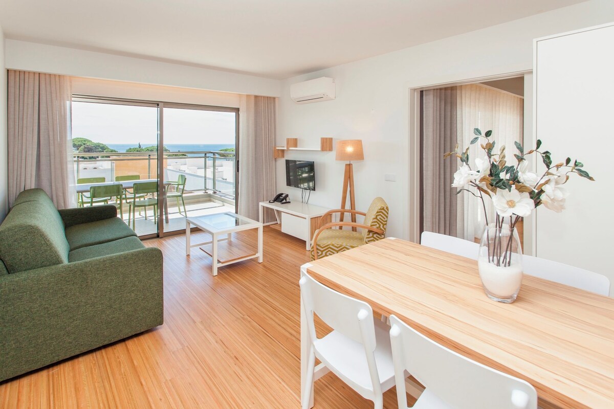 A modern hotel room with a balcony, a dining area, and a TV.