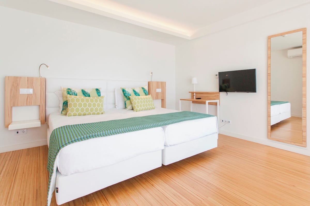 Un dormitorio moderno con cama, mesitas de noche, televisor y espejo.
