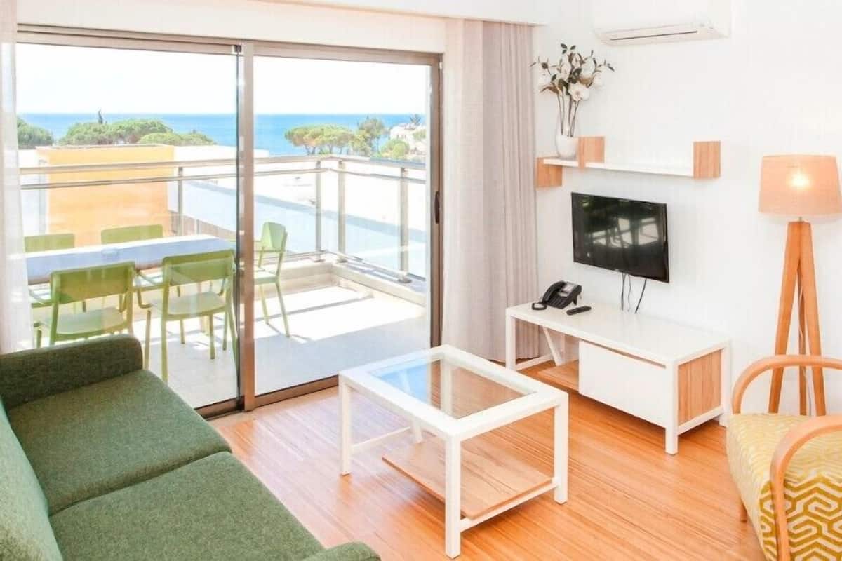 Una habitación de hotel moderna con balcón, televisor, escritorio y sofá.