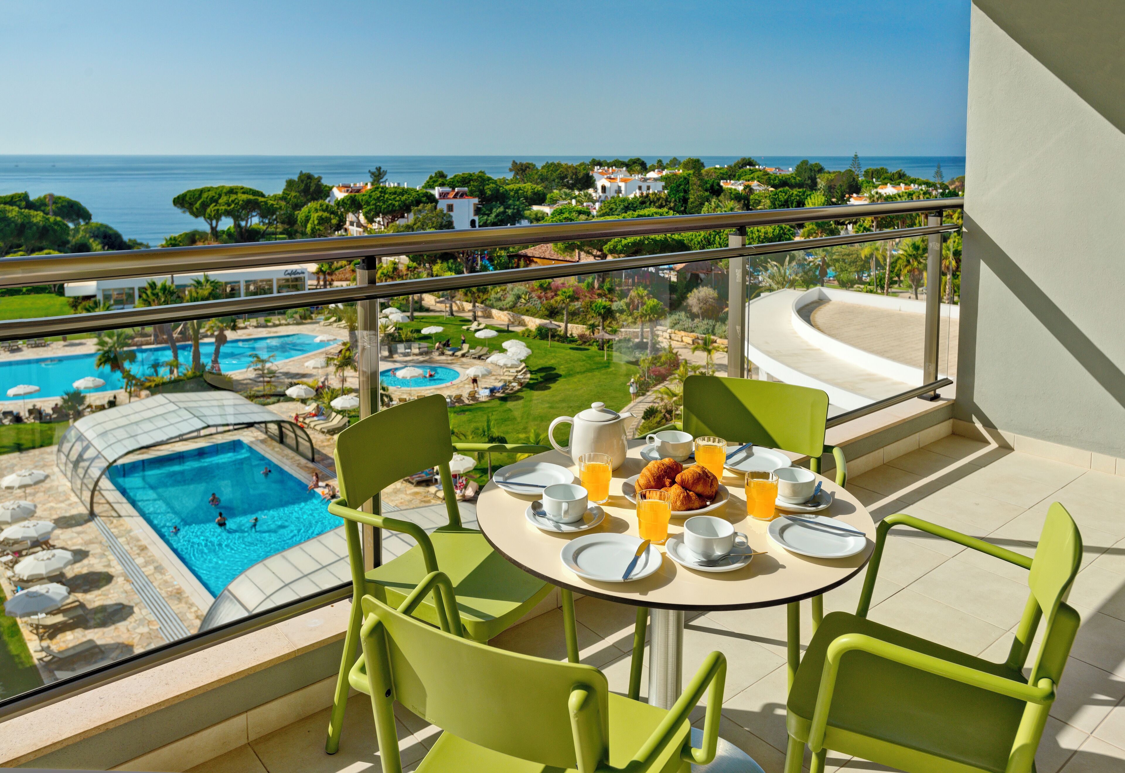 Un balcone con un tavolo apparecchiato per la colazione, vista su una piscina e una spiaggia.