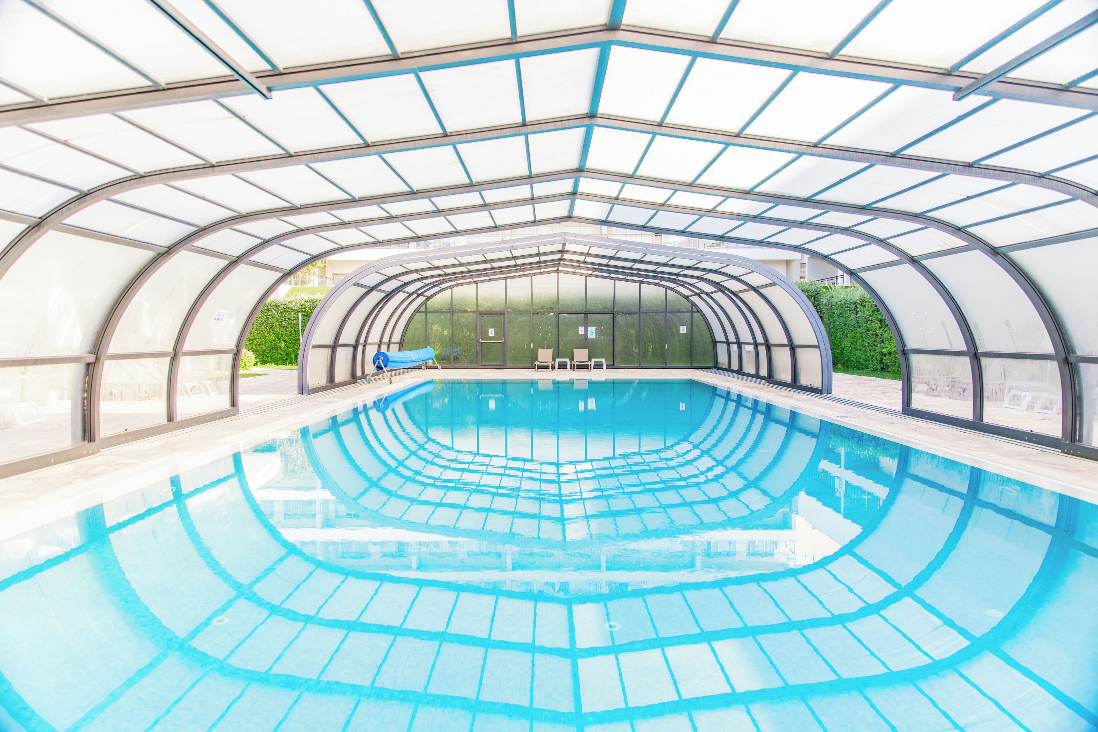 Une piscine couverte dotée d’un toit en verre offrant une vue dégagée sur la végétation environnante.
