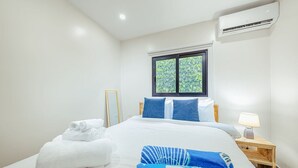Et hotelværelse med seng, vindue, klimaanlæg, et sengebord med lampe og pænt foldede håndklæder.