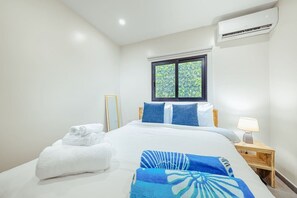 Ein Hotelzimmer mit Bett, Fenster, Klimaanlage, Nachttisch mit Lampe und ordentlich gefalteten Handtüchern.