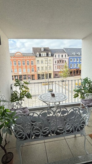 A balcony with a metal table and chairs, potted plants, and a view of colorful buildings. - Full City Apartment at Spittel (square) pedestrian zone Ideal for couples (Bitburg)