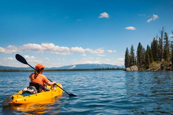 A person kayaking on a calm lake with a clear sky and mountains in the background.