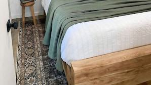 A neatly arranged bedroom with a wooden bed, green bedding, a decorative rug, and a painting on the wall. - Glamping Cabin | Best Bay Views | Near Restaurants (Gouldsboro)