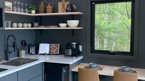 A modern kitchen with grey cabinets, a built-in dishwasher, and a dining area with two chairs. - Bay Front A-Frame | Near Birch & Bunker`s Harbor (Gouldsboro)