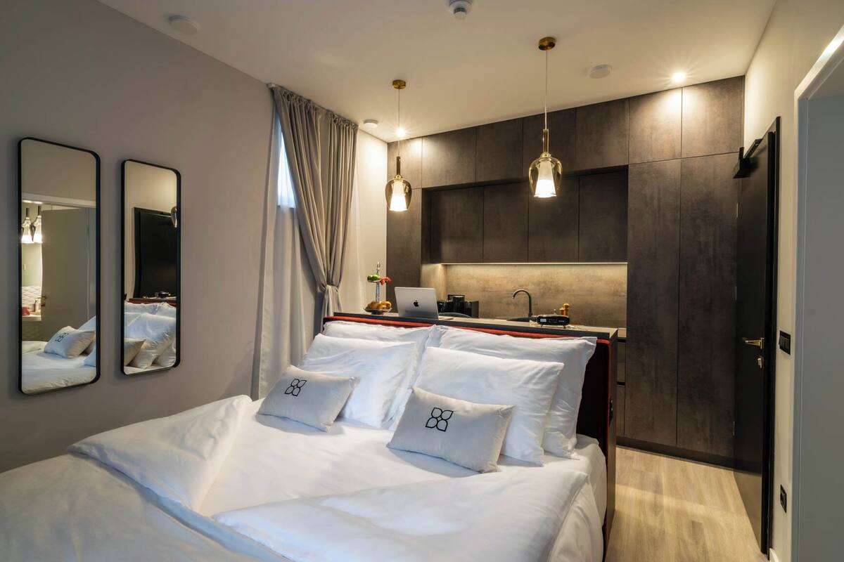 Ein modernes Hotelzimmer mit Bett, Nachttischen, einem Laptop, einem Spiegel und einem Kleiderschrank.
