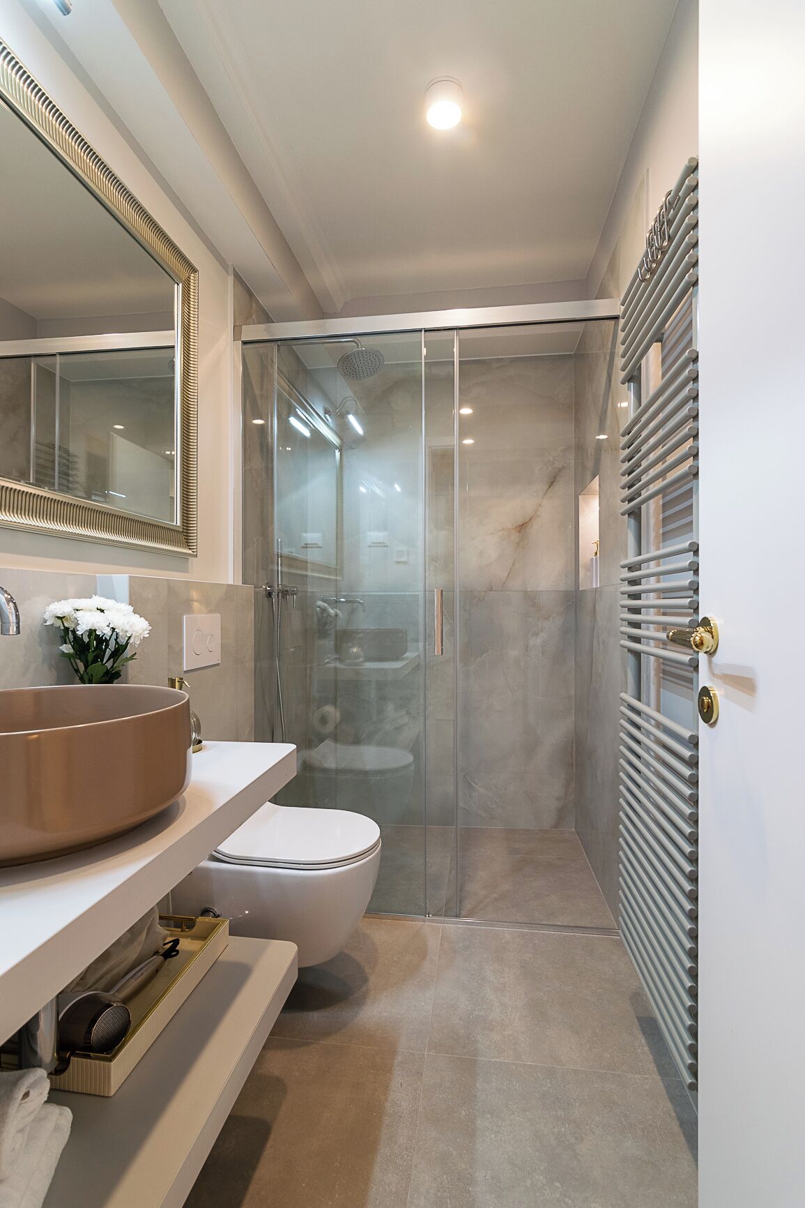 Une salle de bain moderne avec un grand miroir, un lavabo rond, des toilettes et une douche à parois de verre.
