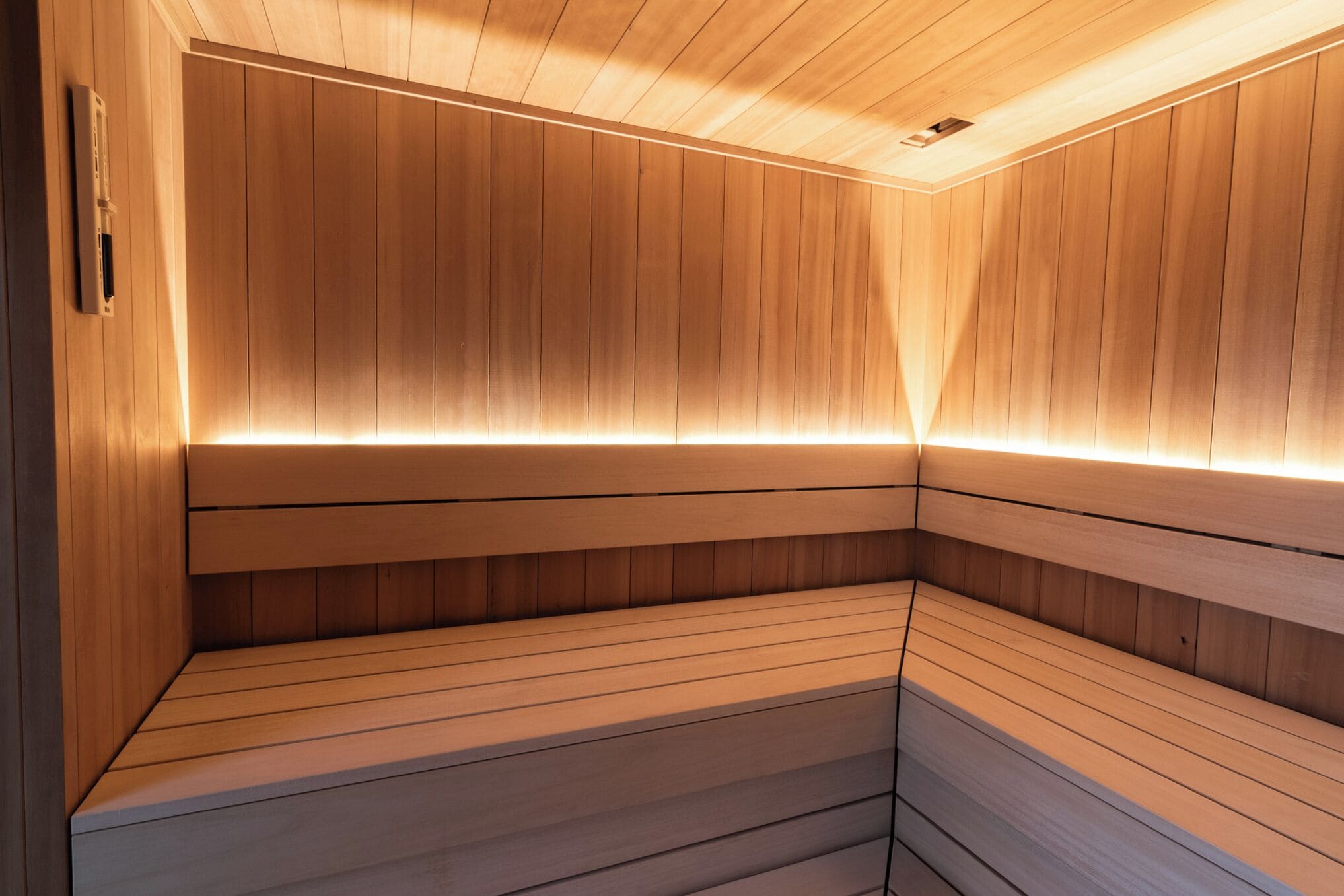 Sauna, jossa on puuseinät ja -lauteet, näkyvissä oleva ilmanvaihtojärjestelmä ja valaistut laudepaikat.
