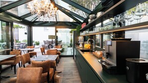 Un restaurante moderno con cerramiento de vidrio, una lámpara de araña, asientos y una barra de café.