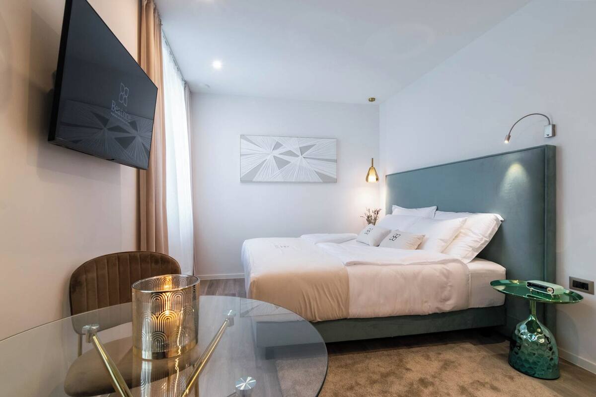 Ein Hotelzimmer mit einem Bett, einem an der Wand befestigten Fernseher, einem Glastisch mit Kerze und einer dekorativen Lampe.