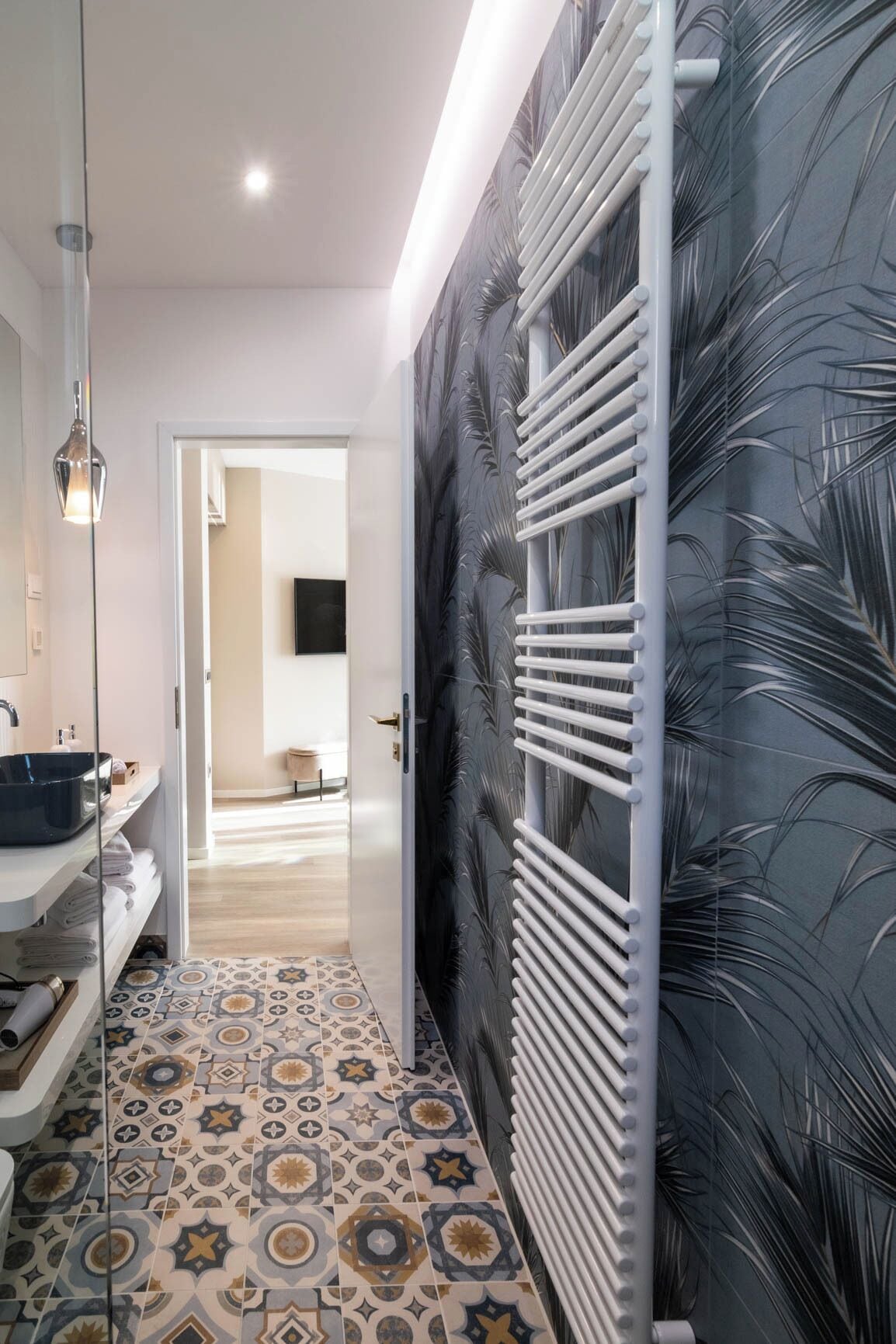 A bathroom with a modern design, featuring a patterned tile floor, a white sink, and a towel rack.