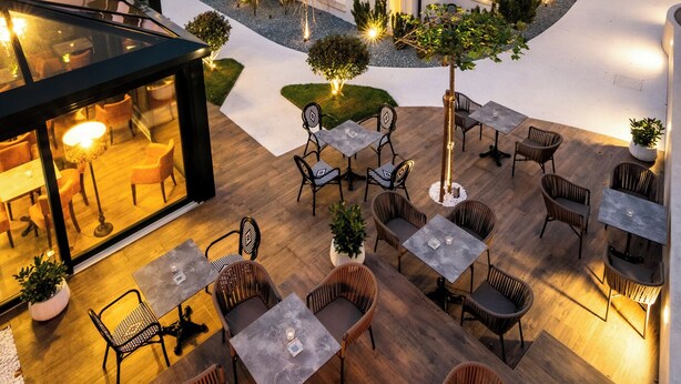 Un edificio moderno con techo inclinado, paneles solares y un patio con mobiliario exterior.