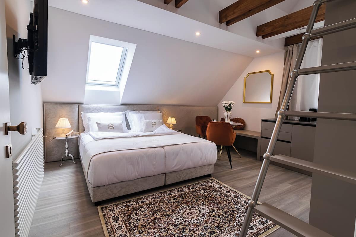 Ein Schlafzimmer mit Bett, Nachttischen, Schreibtisch, Stuhl, Fenster und einer Leiter.