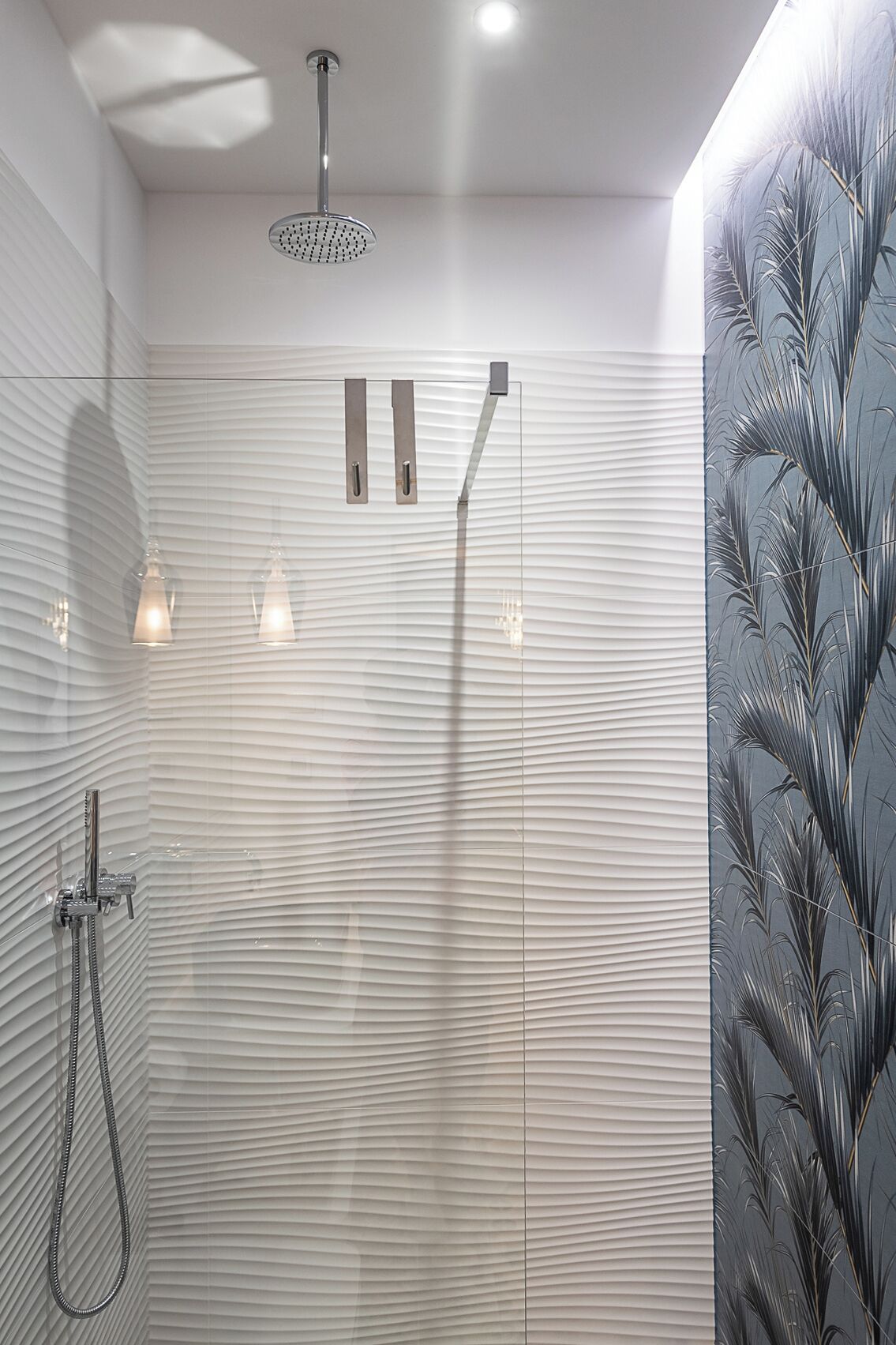 A modern shower with a rain showerhead and handheld showerhead, a towel rack, and a textured wall.