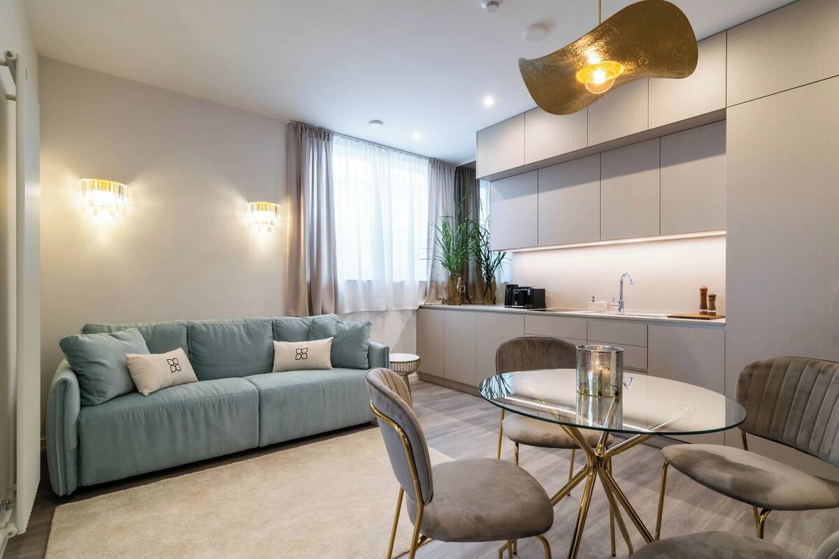 Ein modernes Wohnzimmer mit einer Couch, Sesseln, einem Glastisch und einer Küchenzeile mit Schränken und einer Spüle.