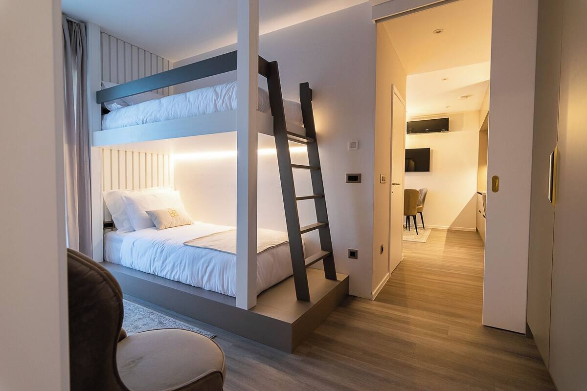 Ein Stockbett mit einer Leiter, ein Stuhl und ein Flur, der in einen Küchenbereich führt.