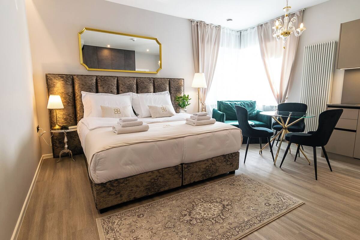 Ein Hotelzimmer mit einem großen Bett, Nachttischlampen, einem Schreibtisch, einem Sessel und Blick auf die Stadt.