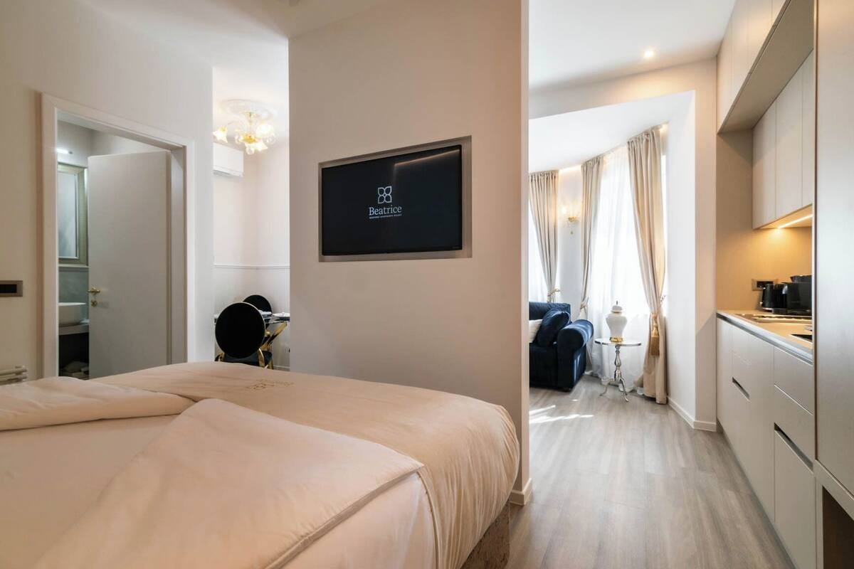 Ein Hotelzimmer mit einem Bett, einem Schreibtisch mit Stuhl, einem an der Wand befestigten Fernseher und Blick auf den Flur.