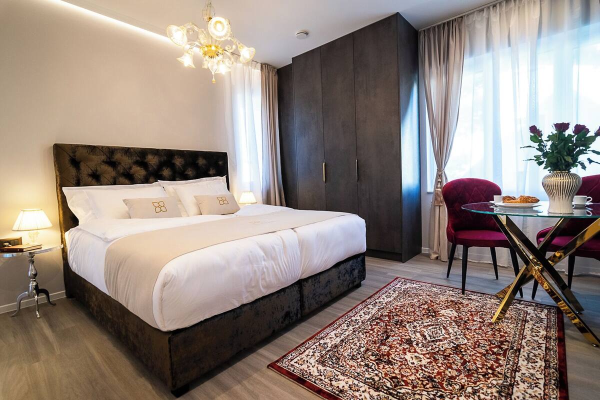 Ein Hotelzimmer mit einem großen Bett, einem dunklen Holzschrank, einem Esstisch mit Stühlen und einer Kristallleuchter.
