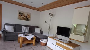 Un salon moderne avec un canapé gris, une table basse en bois, un téléviseur et un meuble contenant de la verrerie.