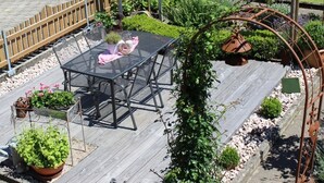 Une terrasse dotée d’une table et de chaises en verre, entourée de plantes en pot et d’une clôture en bois.
