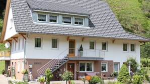 Une maison à deux étages, dotée d’un toit en pente, d’un porche à l’avant et d’un escalier menant au deuxième étage.