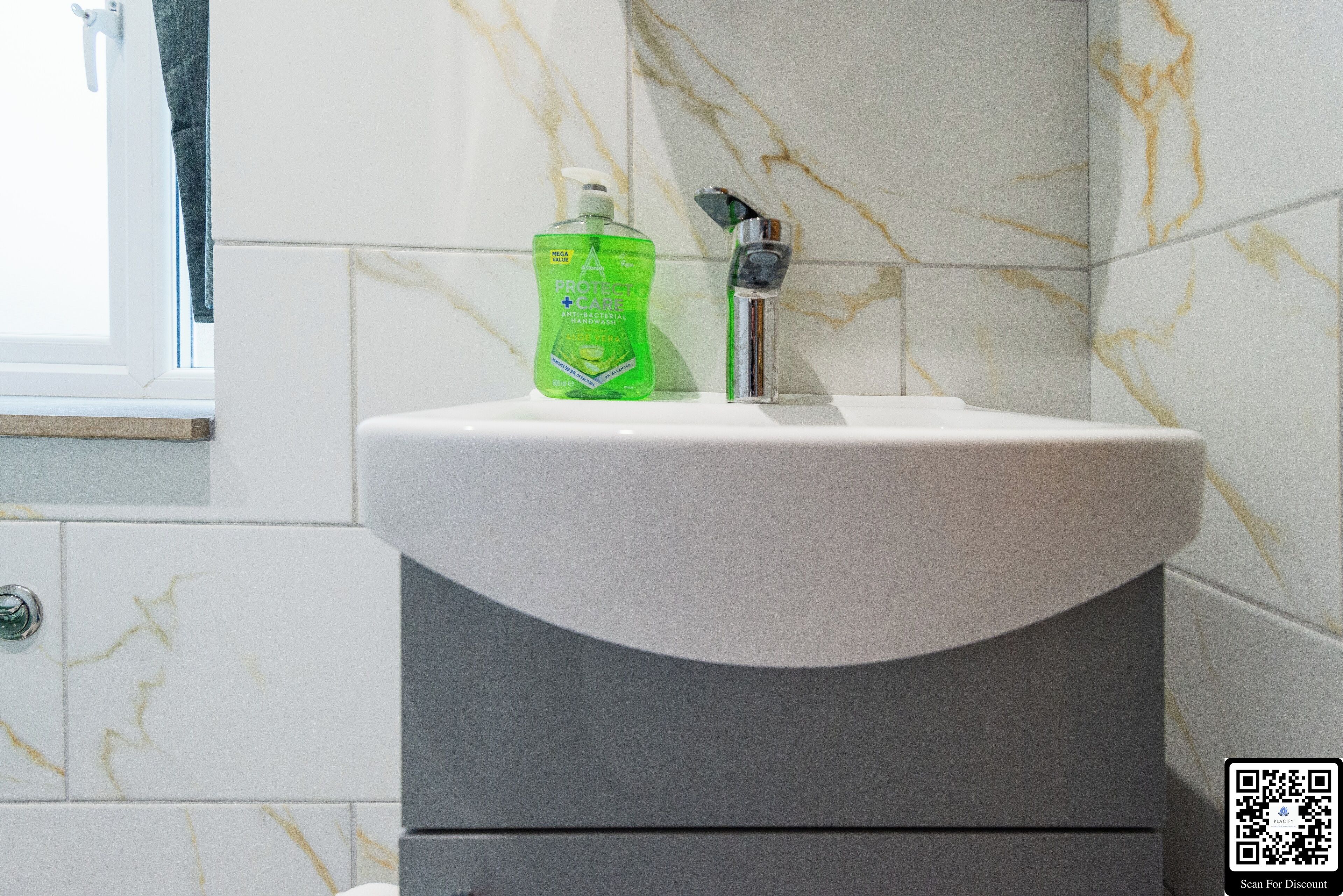 A bathroom with a white sink, a green bottle of hand soap, and a chrome faucet.