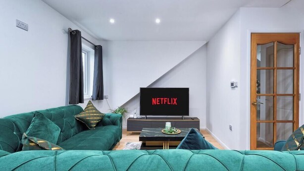 A living room with a green sofa, a flat-screen TV, and a wooden door.