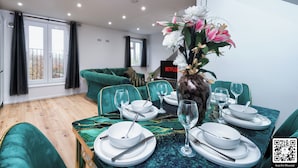 A dining area with a table set for four, green upholstered chairs, and a vase with flowers.