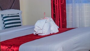 Una camera d'albergo con un letto rifatto, una coperta rossa e un asciugamano bianco sul letto.