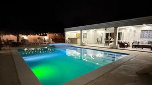 Ein Nachtblick auf einen Poolbereich mit Liegestühlen und einem Gebäude mit Bar und Sitzgelegenheiten.
