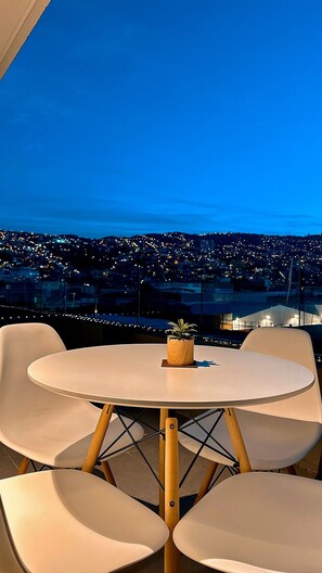 A round table with four chairs, a small potted plant, and a view of a cityscape at dusk. - Vistas de Valparaíso 617 (Valparaíso)