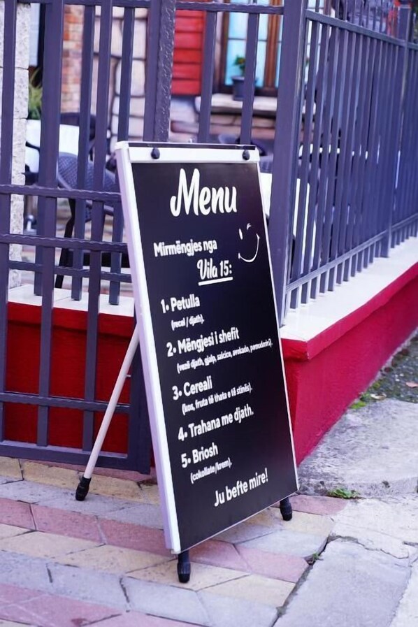 A menu board outside a building with a black background and white text listing food items. - Vila 15 by Nam Nam (Tirana)
