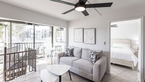 Un salon moderne avec un canapé, une table basse et un ventilateur de plafond. Il y a un balcon avec une balustrade et une vue sur l’extérieur.