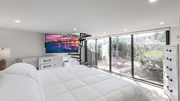 Une chambre moderne avec un grand lit, un téléviseur fixé au mur et une vue sur un pont, visible à travers de grandes fenêtres.