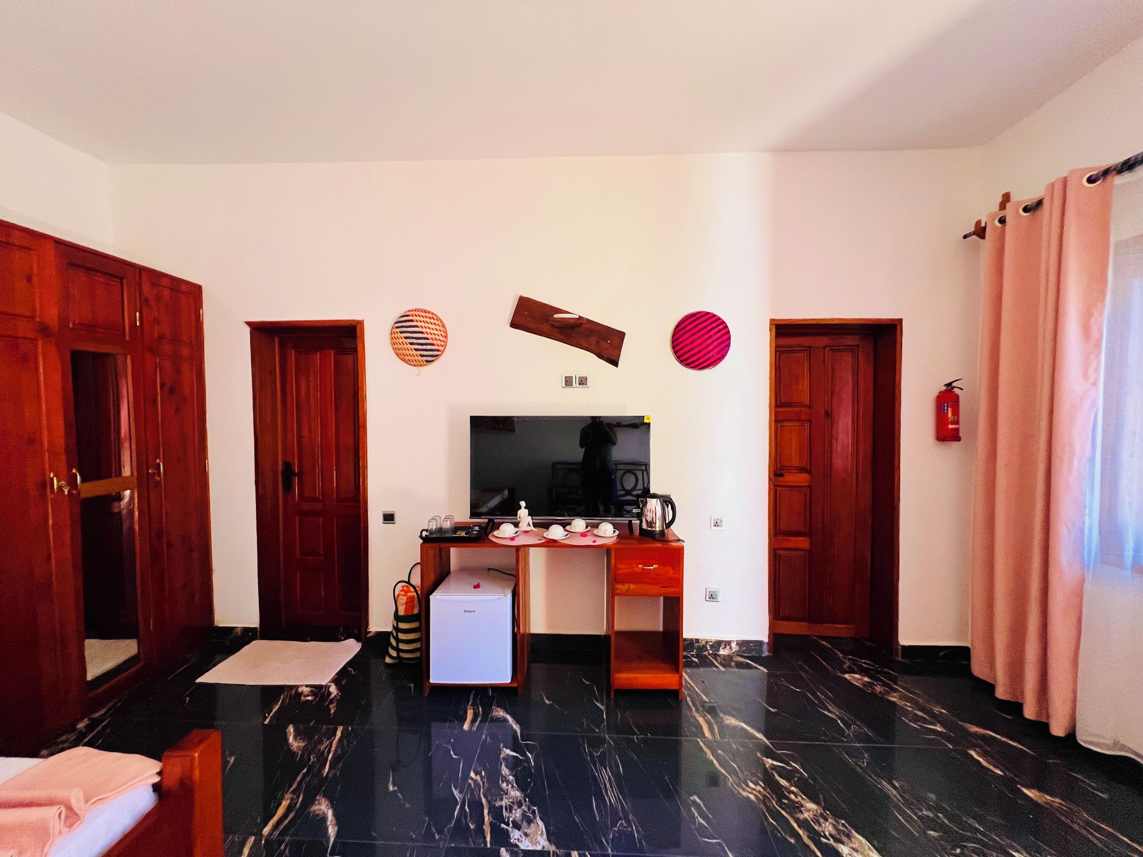 Una habitación con una cama, un escritorio con computadora, una cafetera y un televisor.