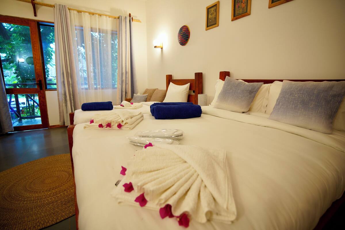 Habitación de hotel con una cama grande, cabecera de madera, un ventanal con cortinas y vistas a zonas verdes.