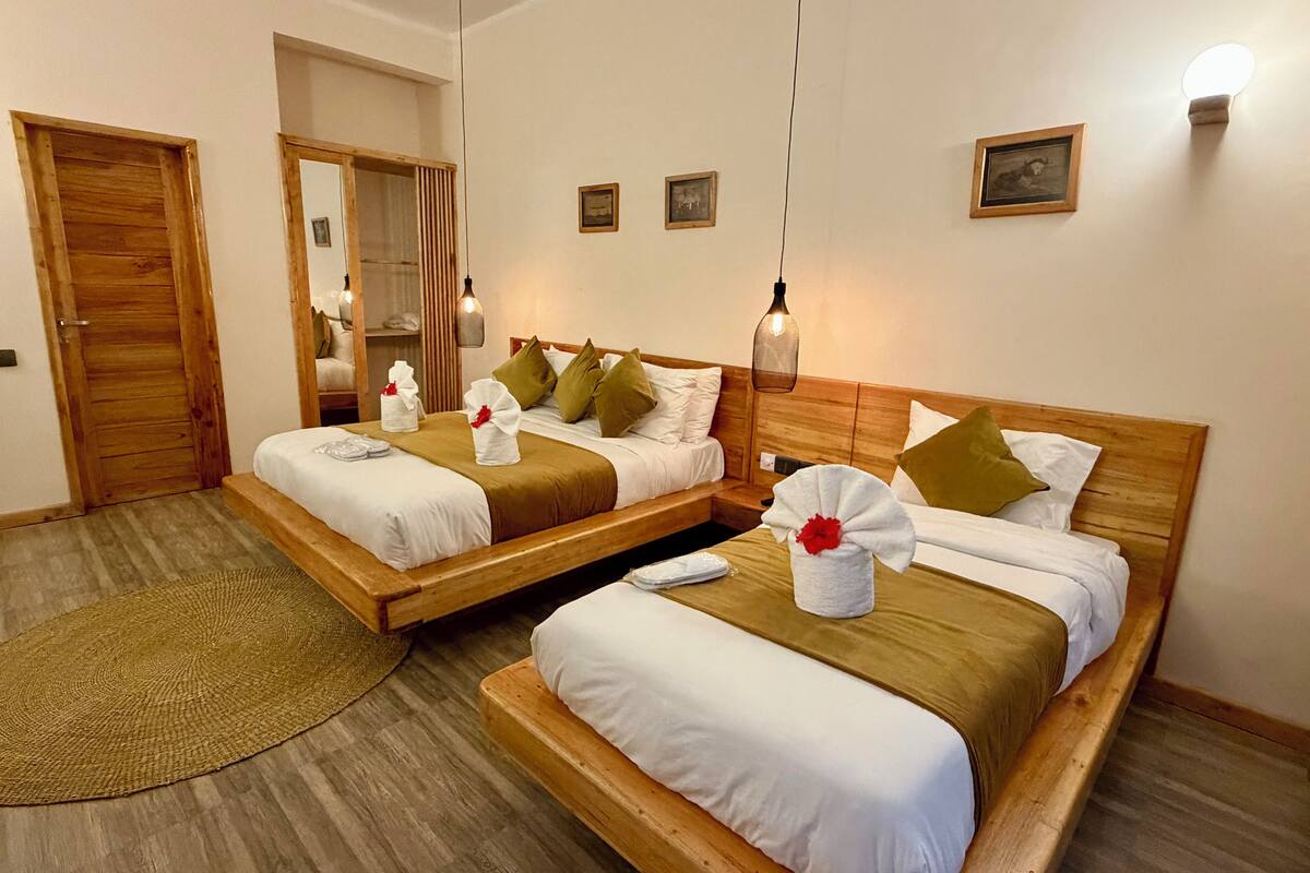 Habitación de hotel con dos camas de madera, una puerta de madera, un espejo y un pequeño cuadro colgado en la pared.