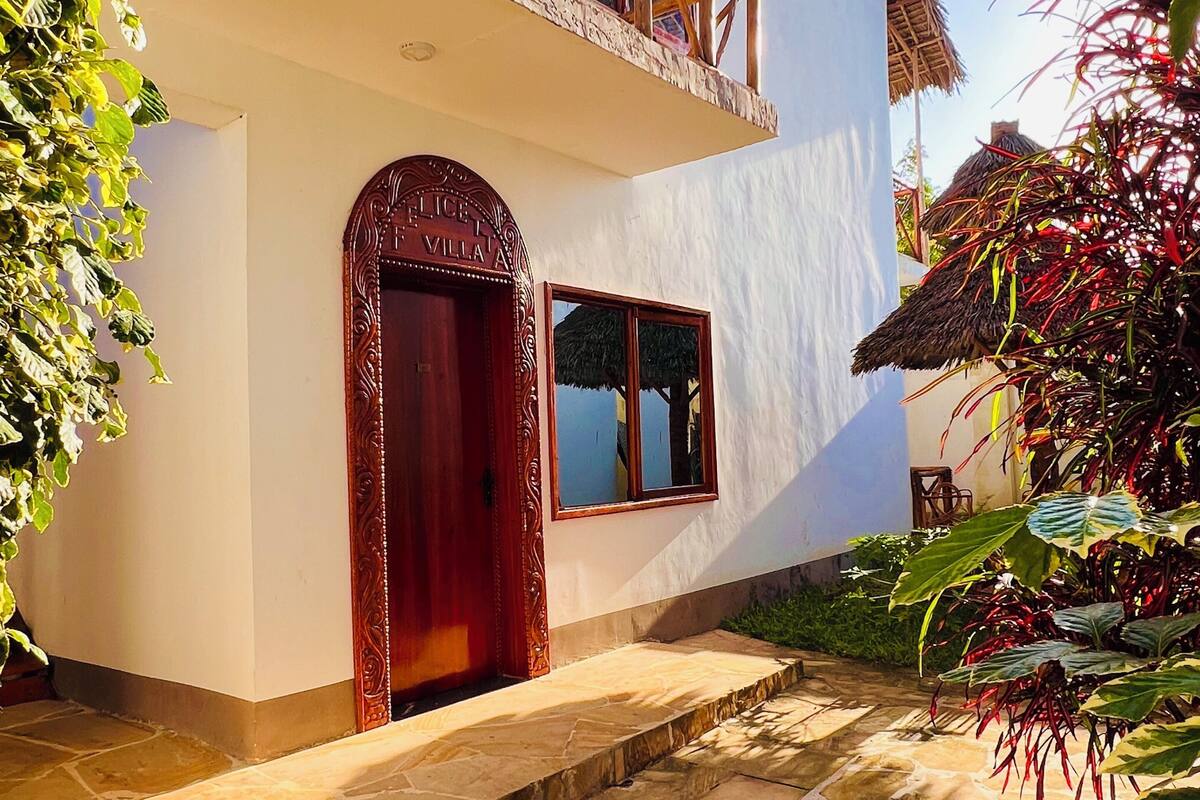 Una villa de dos pisos con un camino de piedra que conduce a la entrada, una puerta de madera y un tejado de paja.