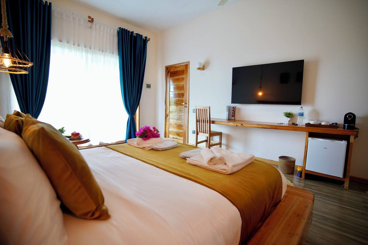 Habitación de hotel con cama, escritorio, televisión y refrigerador pequeño.