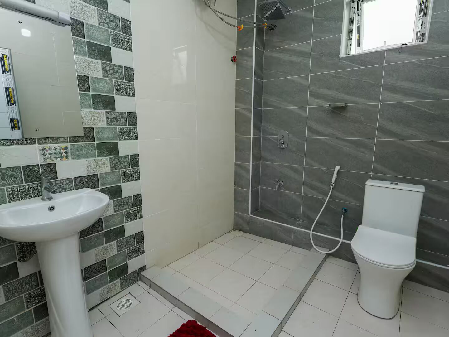 A bathroom with a white sink, a shower with a grey tiled wall, and a toilet.