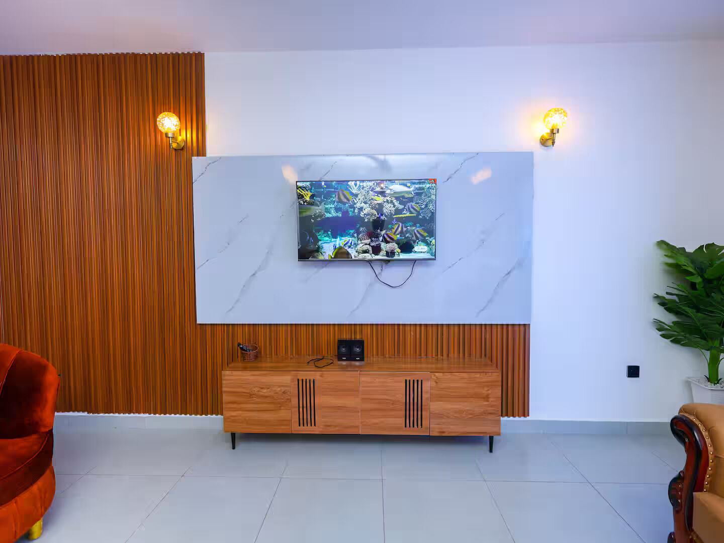 A modern living room with a flat-screen TV mounted on a white marble wall, wooden paneling on the left, and a wooden entertainment unit below.