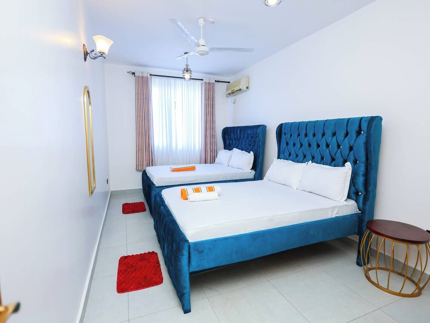 A hotel room with two beds, a ceiling fan, an air conditioning unit, and a small round table.