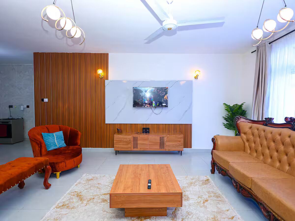 A modern living room with a wooden coffee table, a red velvet sofa, a brown leather sofa, and a wooden cabinet with a TV mounted on the wall.