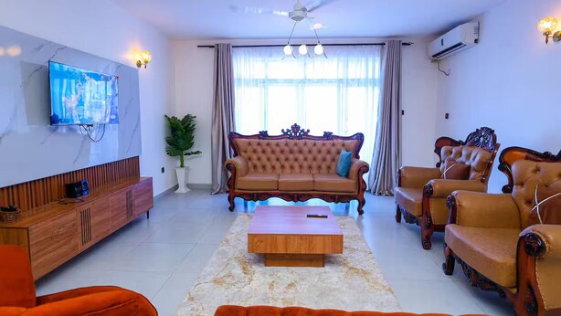 A living room with a sofa, armchairs, a coffee table, a TV, and a ceiling fan. - Homes by Pesh - Nyali, 2 bedroom - Mombasa. (el doret)